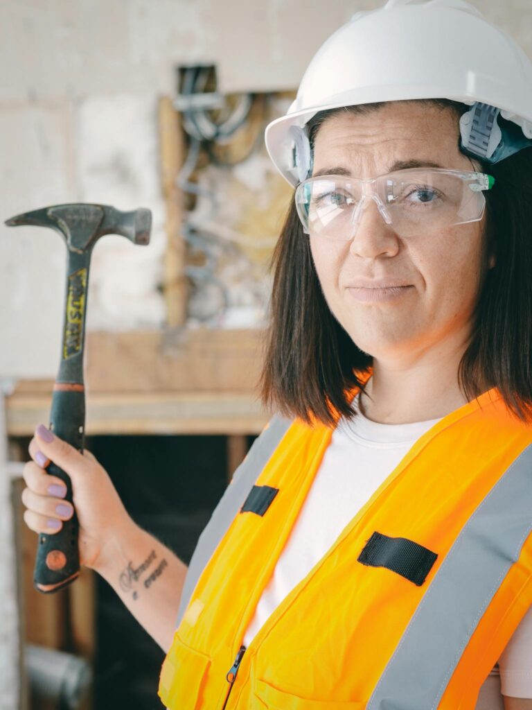 Close-up of a female construction worker wearing safety gear and holding a hammer.