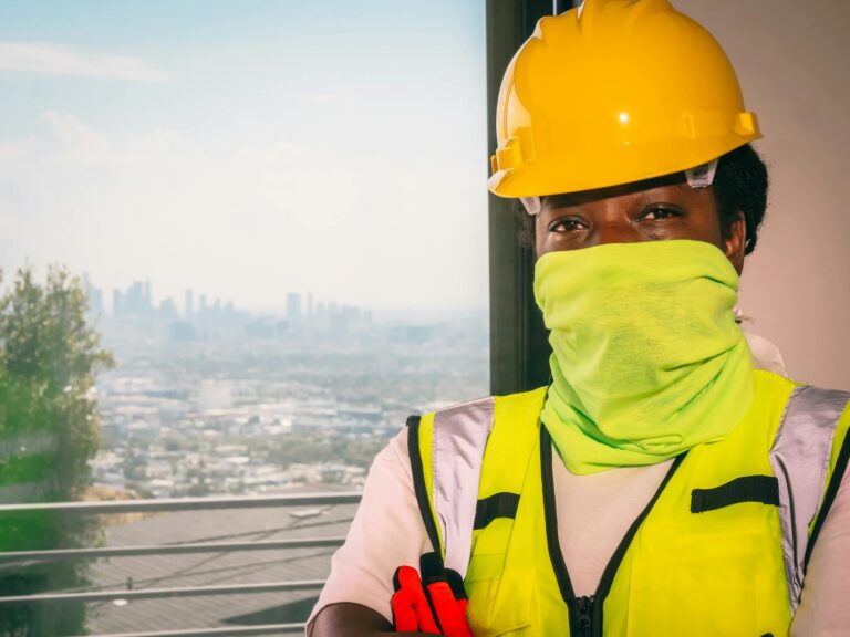 Construction worker in safety gear with covered face and hardhat overlooking cityscape.